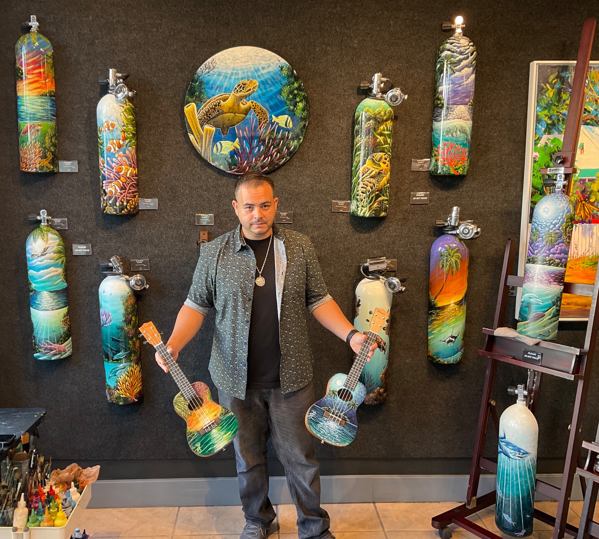 Danilo Alayon standing in a gallery with his painted dive tanks